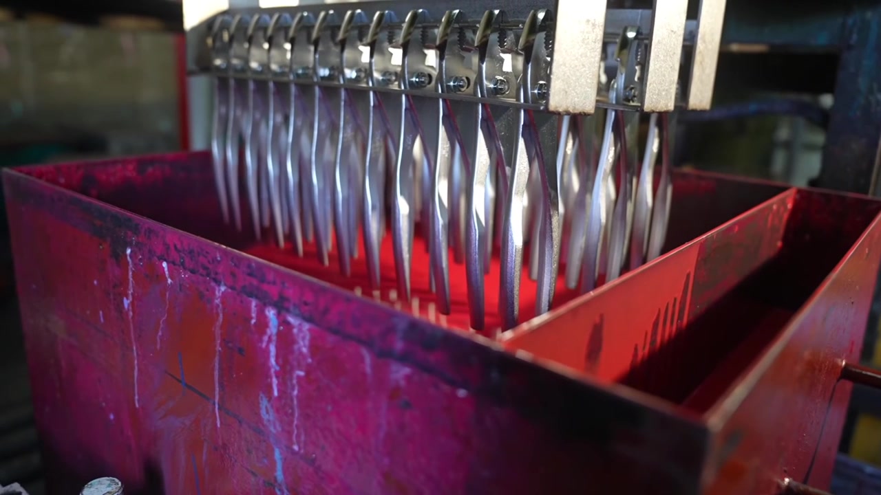 File di pinze finite sospese sopra un contenitore di raccolta rosso dopo il processo di galvanizzazione