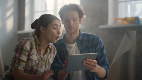 Happy-couple-discussing-design-ideas-indoors.-Woman-pointing-to-tablet-screen.