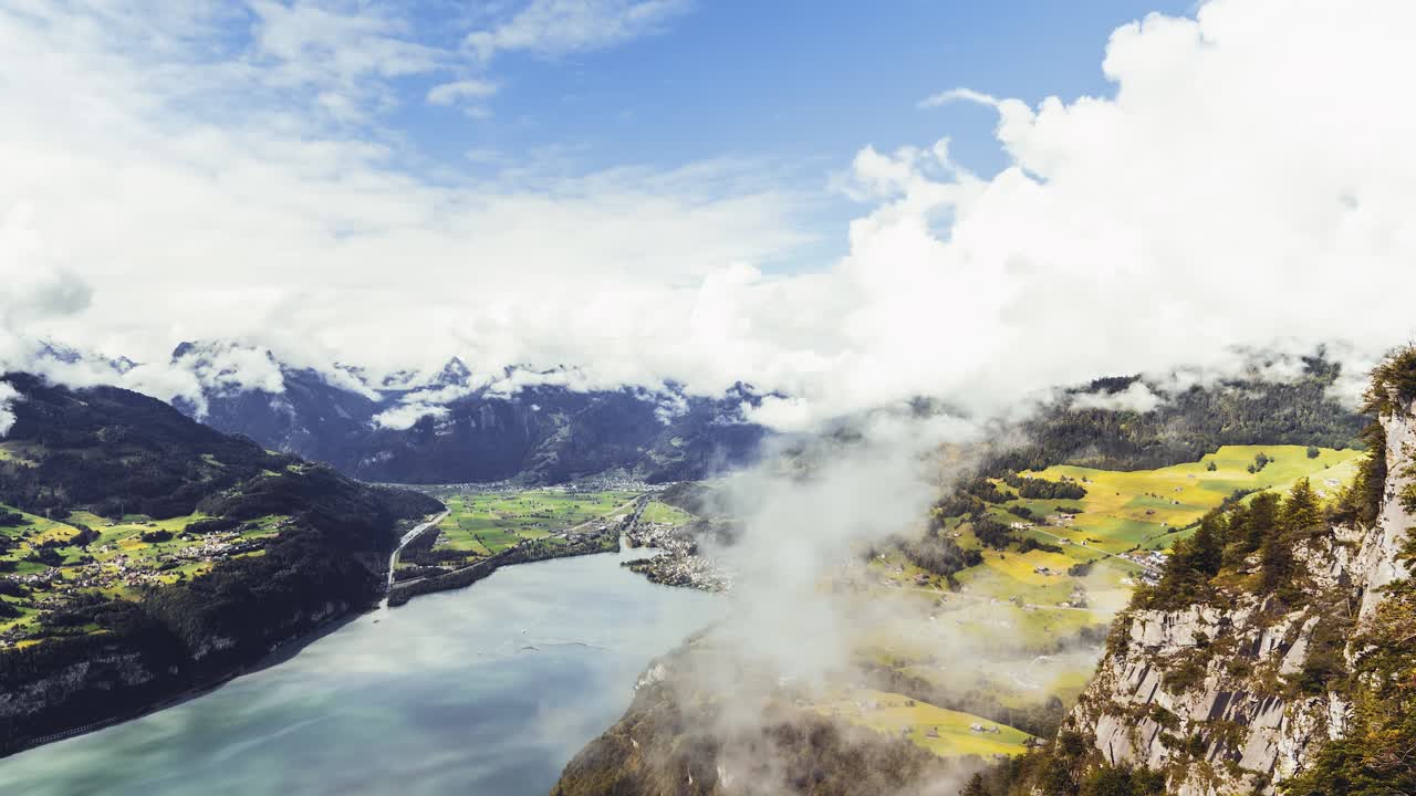Sweeping view of Lake Walen (near Amden, St. Gallen, Switzerland) from a cliff vantage point. A lush valley and turquoise lake, framed by towering peaks and dramatic rolling clouds. (moving timelapse)