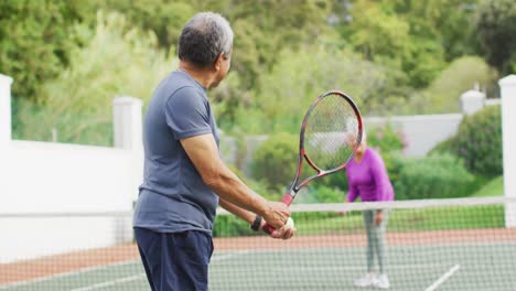video de un hombre mayor biracial feliz sosteniendo una raqueta y comenzando el partido en la cancha de tenis