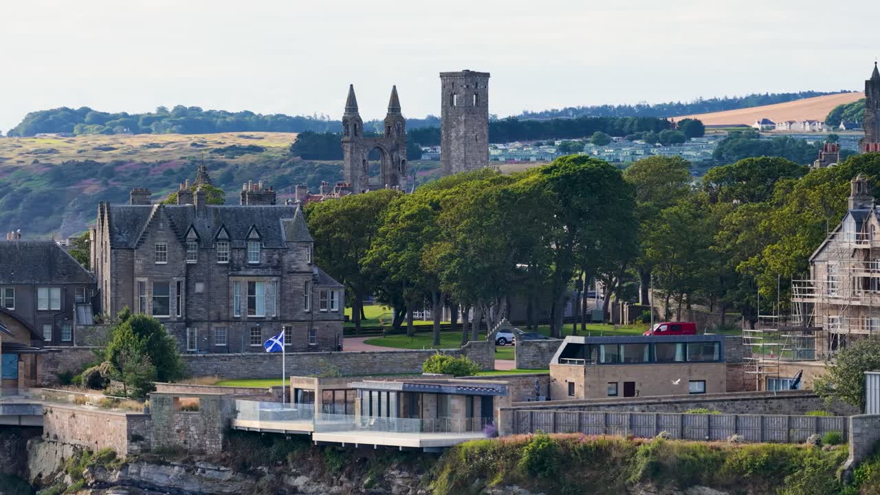 Drone camera slowly pans historic cathedral ruins, university buildings, and coastline in daylight