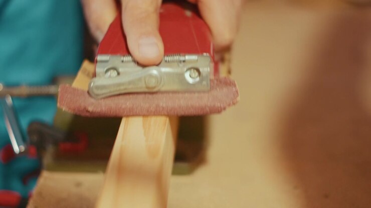 Close-up of a hand using a red sanding block to smooth a wooden plank clamped in a vise. Authentic DIY woodworking footage for craft, carpentry and maker projects