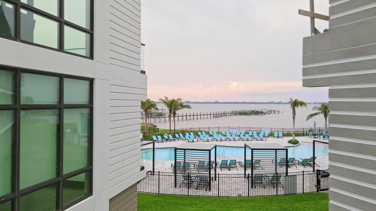 건설 현장에서 시작한 4k 드론  ⁇ 이 2개의 건물을 통과하고 수영장을 지나 해안 근처의 부두와 도크와 함께 바다 물로 향합니다.