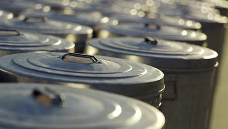 Steel-trash-bins-stacked-together-in-an-endless-loop.-Sunlight-illuminates-shiny-metal-lids-on-a-vast-field-full-of-containers-with-garbage-waste.-Symbol-of-growing-pollution-and-rubbish-outgrowth.