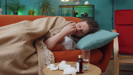 a sick man lying on a couch with a blanket and tissues