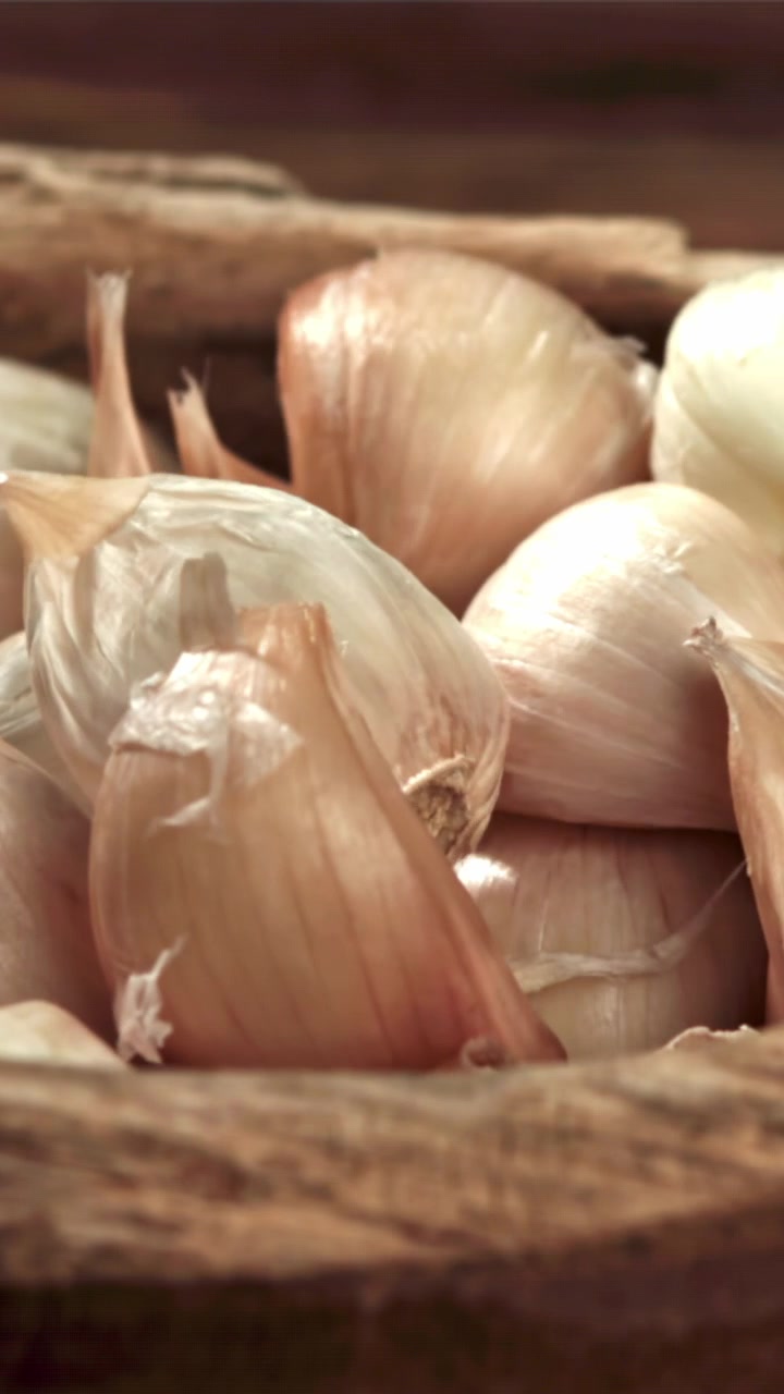 Spicchi d'aglio che cadono in una ciotola di legno rustica al rallentatore
