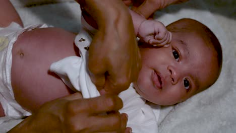 adorable 2 month old indian baby gently getting vest put on by hands of mother after having bath