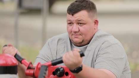 an overweight man is working out on an outdoor simulator doing arm exercises an overweight man working out on an outdoor simulator doing arm exercises a fat man trains his arms while sitting on the exercise machine exerciser for hands