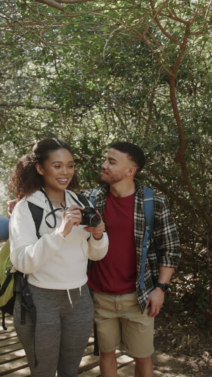 Vertical video of biracial couple taking pictures in forest, slow motion