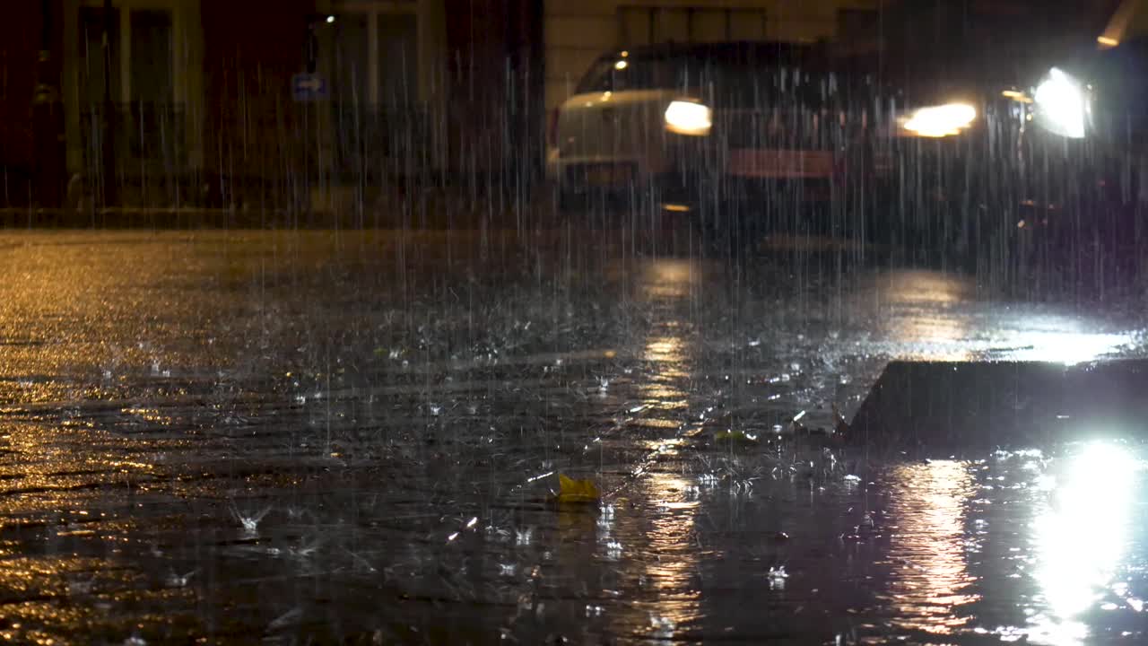 Heavy rain on street pavement at night. Car passing by.