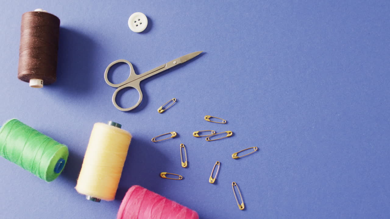 Video of scissors, safety pins, a button and reels of thread on blue background with copy space
