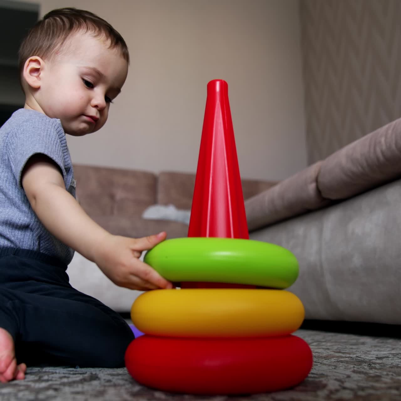 Cute Caucasian kid playing with toy pyramid. Child plays on the floor at home. Black cat at backdrop