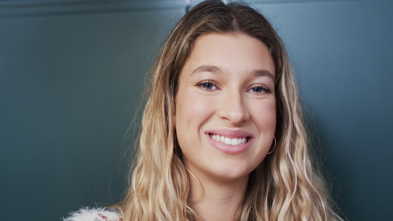 retrato de una feliz mujer biracial con cabello rubio en la cocina en casa, en cámara lenta
