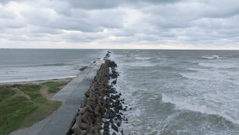 aerial establishing view of port of liepaja concrete pier , autumn storm, big waves splashing, overcast day, wide drone shot moving forward