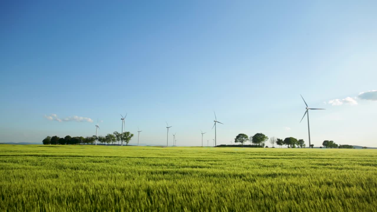 Wind Turbines Standing In The Lush Field In Zlotoryja, Poland Against The Bright Blue Sky - wide trucking shot