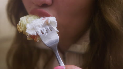 Close-up of hand holding fork and knife, cutting croissant with whipped cream and fruit topping in cozy cafe. The relaxed, enjoyable moment of eating in a soft, inviting atmosphere