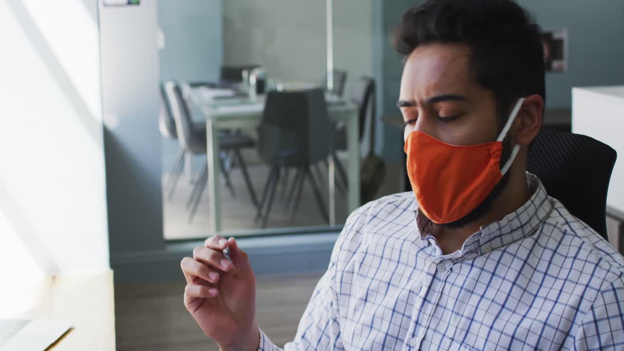 Uomo mediorientale che indossa una mascherina e prende appunti in un ufficio moderno