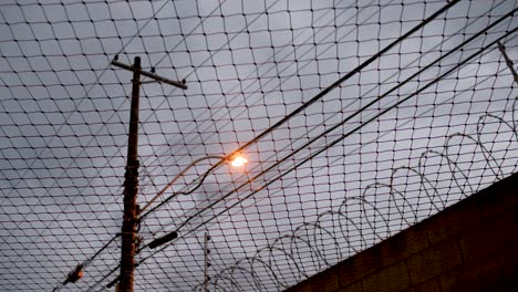 Street-light-and-silhouette-of-barbed-wire-fence-through-netting-at-dusk