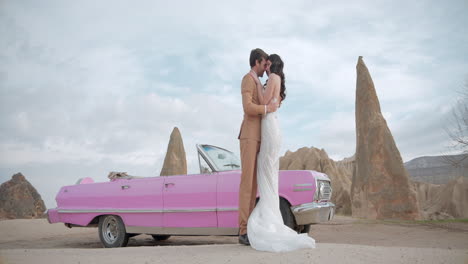 romantic couple kissing near pink vintage car in cappadocia