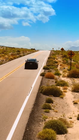 catching up with a black car driving by the highway in desert. drone raising above the dry valley in nevada surrounded by mountains at backdrop. vertical video