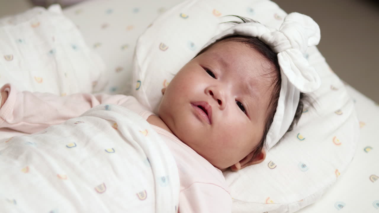 Puzzled baby in pink outfit with white bow squirming on the bed. Playful and curious moment of a baby girl captured with softness and charm