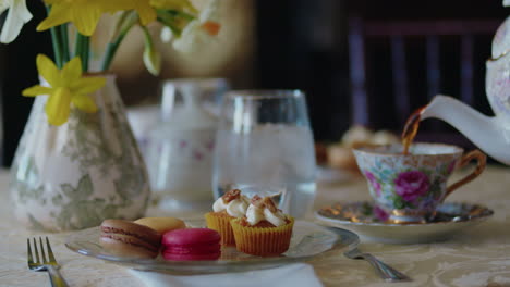 elegant table is set with yellow daffodils and pink macrones and the tea is poured into the cup