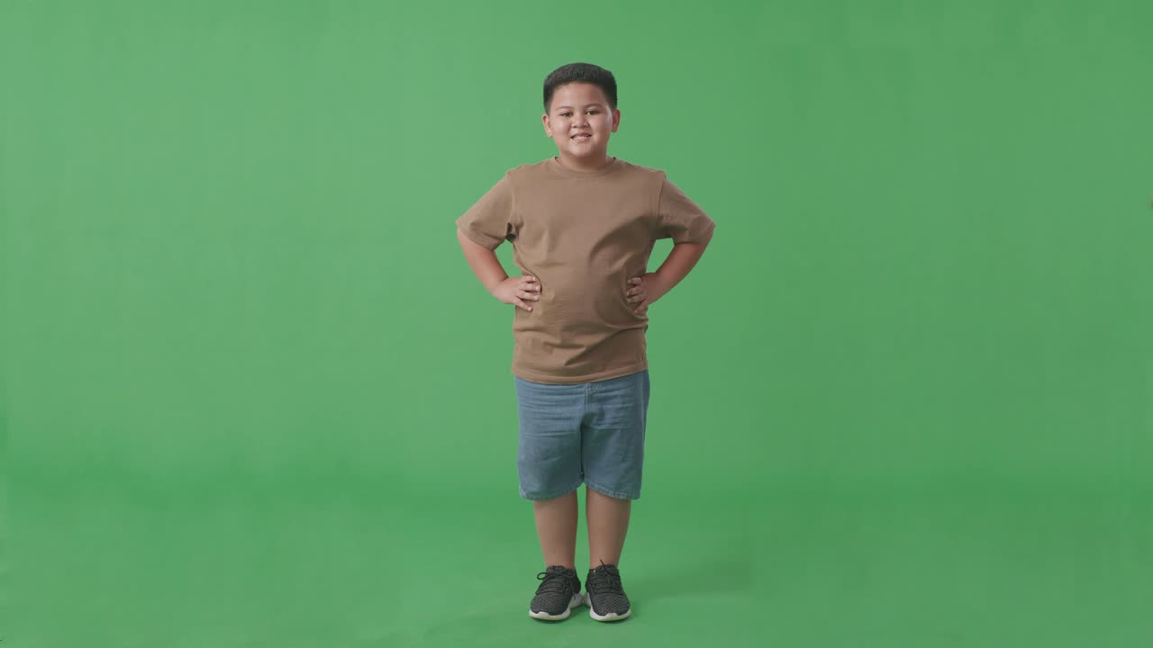 스튜디오의 녹색 스크린 배경에서 따뜻하게 미소 짓는 아시아 소년의 몸이 가득 차 있습니다.