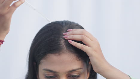 close up shot of a young lady applying minoxidil on her head and massaging for androgenic alopecia hairloss treatment.