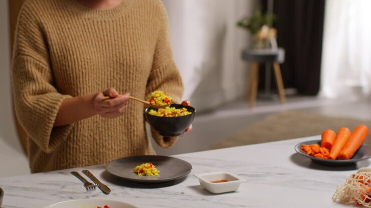 Primo piano di una donna a casa in cucina che prepara un pasto vegetariano o vegano sano a base di pasta orzo e pomodori arrostiti.