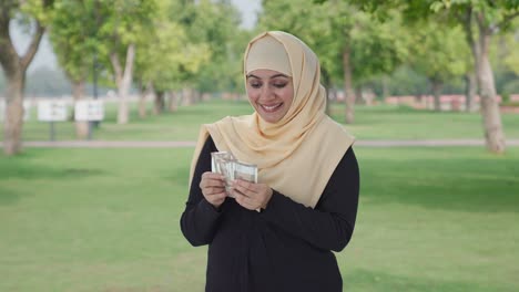 happy muslim woman counting money in park