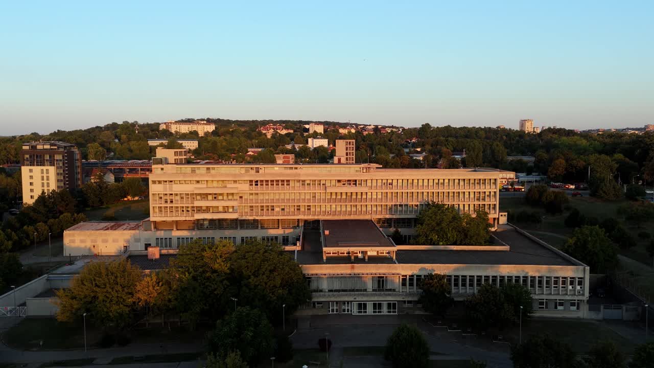 Aerial drone view of Belgrade, Serbia, showcasing brutalist architecture at sunset. Concrete buildings glowing in warm light symbolize postmodern urban identity
