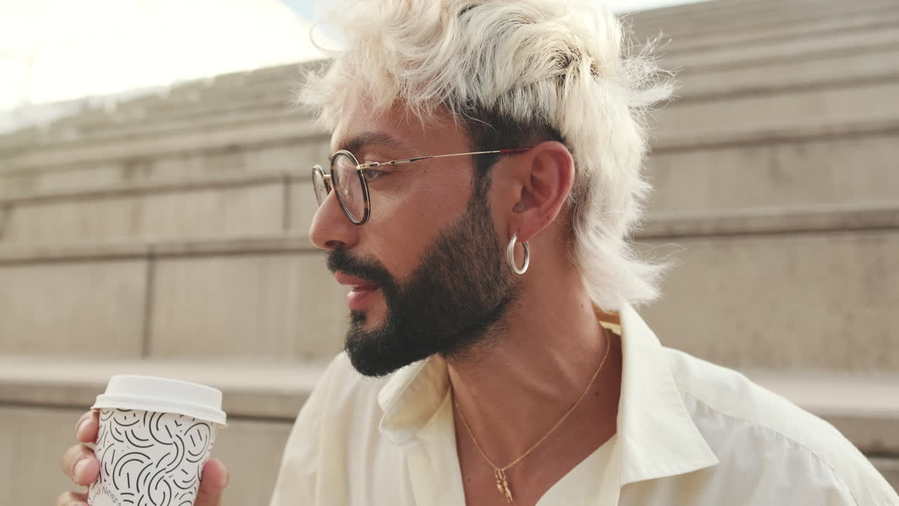 Uomo alla moda con capelli decolorati e barba che beve caffè all'aperto