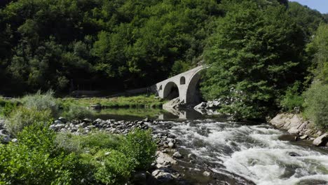 approaching drone shot showing the flowing rapids of arda river and the arches of the devil's bridge also called the dyavolski most located in ardino at the foot of rhodope mountains in bulgaria