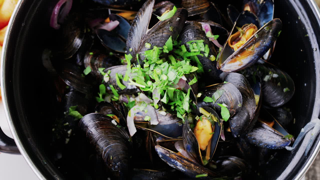 Close up of multiple steamy mussels in a pot with parsley on top