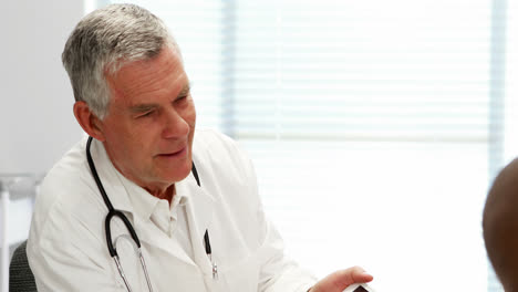 Male-doctor-using-digital-tablet-while-interacting-with-patient