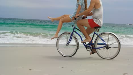 side view of caucasian couple riding a bicycle on the beach 4k