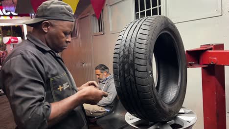 Mecánico-Afroamericano-Arreglando-Un-Neumático-De-Coche-En-El-Taller