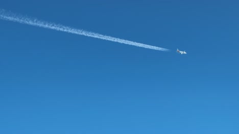 a twin-engine jet and its contrail crossing left to right in a blue sky. aerial footage taken from another jet cockpit flying bellow.