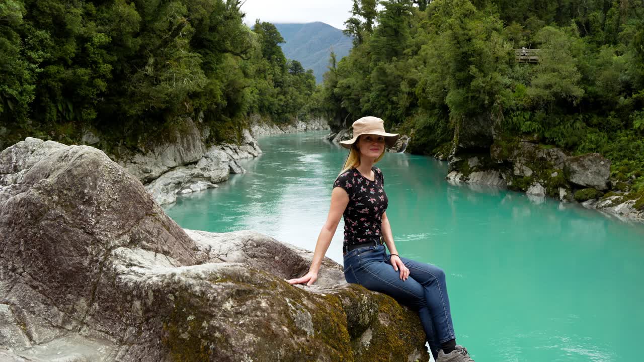 Woman sitting on a rock by a beautiful turquoise river in New Zealand