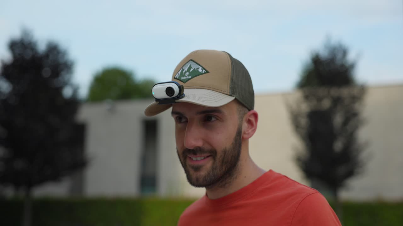 Vlogger Turning On Action Camera Attached On Brim Of Baseball Cap Outside
