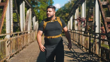 joven viajero con mochila caminando por el viejo puente oxidado al aire libre en un soleado día de verano en cámara lenta