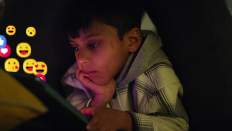 niño joven acostado en el sofá en casa por la noche mirando una tableta digital con emojis de gráficos en movimiento que muestran múltiples notificaciones de redes sociales o mensajes gustando y reaccionando al contenido en línea