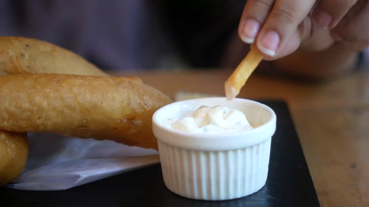 Hånd som dypper pommes frites i en saus