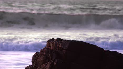 Ocean-waves-splash-crash-in-background-against-Big-rock-in-slow-motion-on-cloudy-day-medium-shot