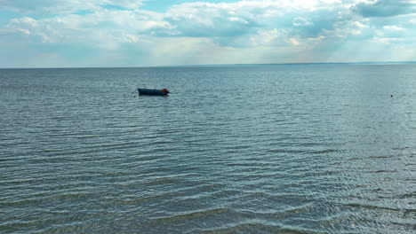 Einsames-Boot,-Das-Auf-Einem-Weiten,-Ruhigen-Meer-Unter-Einem-Himmel-Schwimmt,-In-Dem-Licht-Durch-Die-Wolken-Strömt