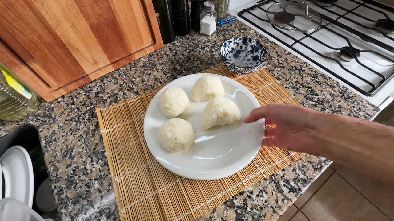 A Hand Places a Plate of Freshly Made Onigiri on the Kitchen Counter - Close Up