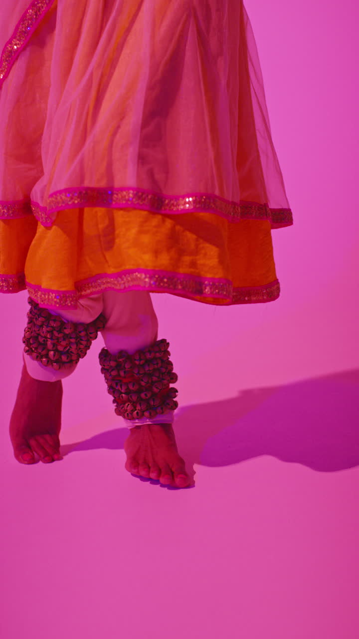 video vertical de primer plano de los pies con campanas de una bailarina de kathak femenina realizando un baile vestida con el vestido tradicional indio contra un fondo púrpura 5