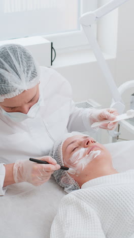 esteticista aplicando una máscara de crema hidratante en el rostro de una mujer joven para rehidratar la piel del rostro