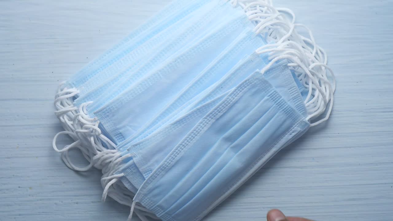 손은 파란색 수술 마스크의 더미를 들고 있습니다.