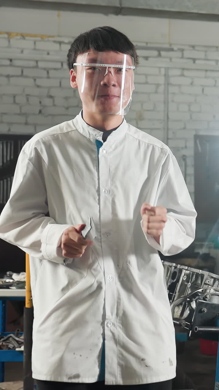 색 실험실 코트와 보호 안경을 입은 두 명의 학생이 기계 작업장에서 함께 춤을 추고, 빛이 실루 효과를 만들어 산업 환경에서 활기차고 재미있는 순간을 포착합니다.